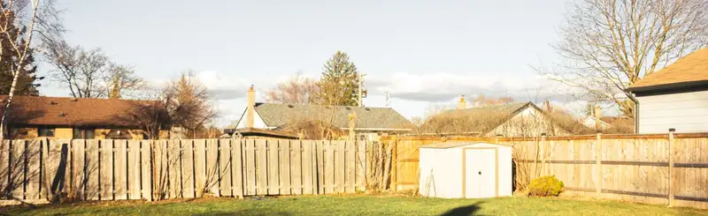A back yard lined with weathered wood privacy fencing, with a small shed in the corner